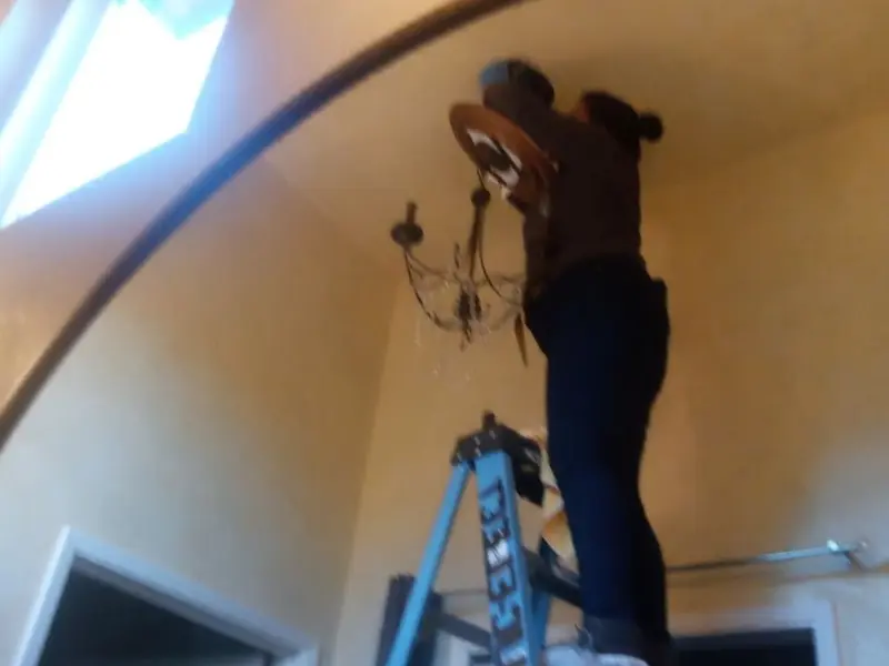 Electrician installing a chandelier in a Needville residence